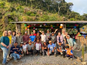 Group photo of people in a rural outdoor setting, with balloons and decorations in the background.